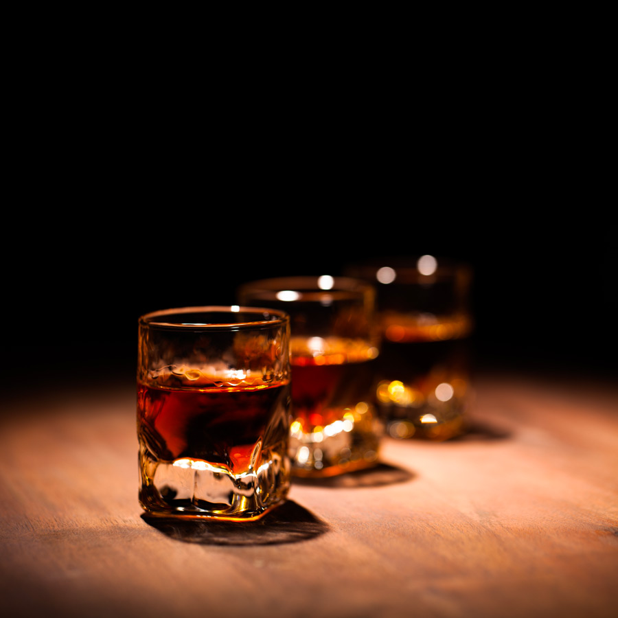 trois verres à spiritueux et remplis de rhum sont alignés sur une table en bois
