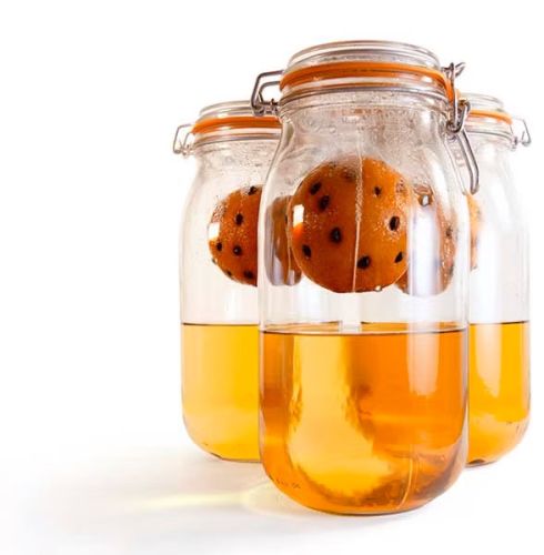 bocaux en verre contenant du rhum ainsi que des oranges suspendues en cours de macération